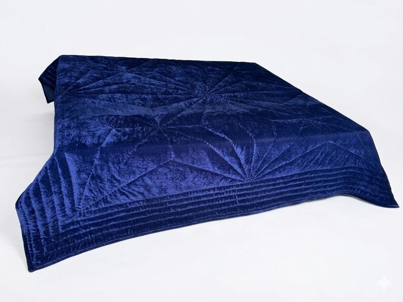May include: A deep navy blue velvet quilt featuring a geometric starburst pattern created by intricate stitching. The fabric has a soft, reflective sheen, and the edges are finished with a wide border containing multiple parallel horizontal lines.