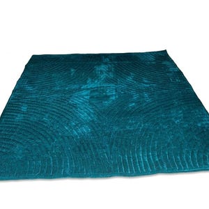 May include: A rectangular teal velvet quilt featuring a repeating fan-shaped stitched pattern across the entire surface. The fabric has a subtle sheen and a deep, saturated color, with visible quilted lines forming curved, semi-circular motifs.