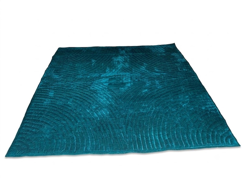 May include: A rectangular teal velvet quilt featuring a repeating fan-shaped stitched pattern across the entire surface. The fabric has a subtle sheen and a deep, saturated color, with visible quilted lines forming curved, semi-circular motifs.