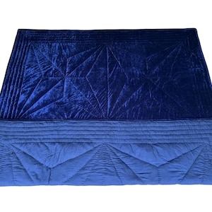 May include: A rectangular quilt featuring a deep navy blue velvet top section with geometric stitched patterns and a lighter blue cotton bottom section with matching linear and triangular quilting details, creating a two-toned blue textile piece.