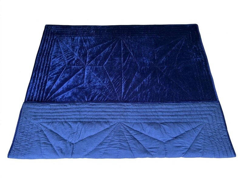 May include: A rectangular quilt featuring a deep navy blue velvet top section with geometric stitched patterns and a lighter blue cotton bottom section with matching linear and triangular quilting details, creating a two-toned blue textile piece.