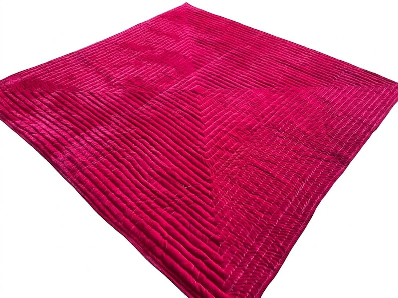 Puede incluir: Una manta fucsia vibrante con un dise&ntilde;o acolchado. La manta presenta una serie de l&iacute;neas paralelas que crean una superficie texturizada. Los bordes est&aacute;n acabados con un patr&oacute;n contrastante, agregando inter&eacute;s visual. La manta es cuadrada.