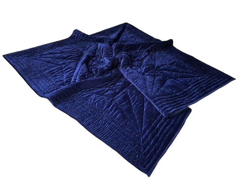 May include: A deep navy blue velvet quilt featuring a geometric star pattern created by intricate channel stitching. The fabric has a soft, plush texture with a subtle sheen, and the edges are finished with a wide, quilted border design.