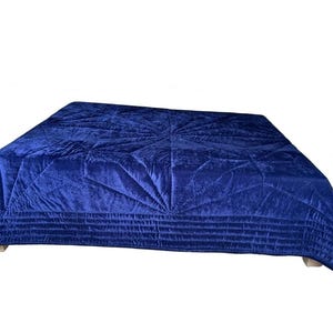 May include: A deep royal blue velvet quilt featuring a central starburst pattern created by intricate stitching. The edges of the quilt are finished with multiple rows of horizontal quilted lines, providing a textured surface across the fabric.