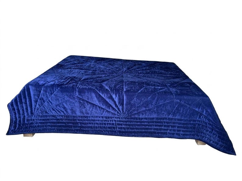 May include: A deep royal blue velvet quilt featuring a central starburst pattern created by intricate stitching. The edges of the quilt are finished with multiple rows of horizontal quilted lines, providing a textured surface across the fabric.