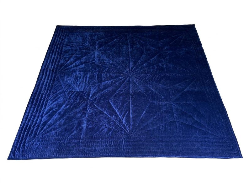 May include: A deep navy blue velvet quilt featuring a geometric star pattern created by intricate stitching. The square textile has a soft, reflective surface with a wide border composed of multiple parallel quilted lines framing the central design.