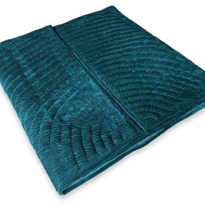 May include: A deep teal velvet quilt featuring a repeating fan-shaped stitched pattern across its surface. The fabric has a soft, textured appearance with a subtle sheen, folded over to display the quilted design and the rich, dark blue-green color.