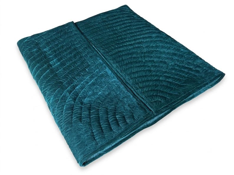 May include: A deep teal velvet quilt featuring a repeating fan-shaped stitched pattern across its surface. The fabric has a soft, textured appearance with a subtle sheen, folded over to display the quilted design and the rich, dark blue-green color.