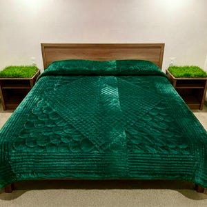 Puede incluir: Una colcha de terciopelo verde esmeralda profundo con un patrón geométrico acolchado que presenta formas de diamante y circulares. La colcha cubre una estructura de cama de madera, flanqueada por dos mesitas de noche de madera con césped.
