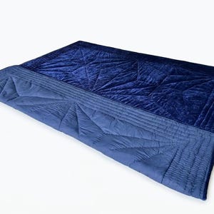 May include: A rectangular quilt featuring a deep navy blue velvet top section and a lighter blue matte fabric bottom section. Both sections are adorned with intricate geometric star-shaped stitching patterns and parallel linear quilting borders.