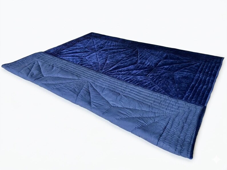 May include: A rectangular quilt featuring a deep navy blue velvet top section and a lighter blue matte fabric bottom section. Both sections are adorned with intricate geometric star-shaped stitching patterns and parallel linear quilting borders.