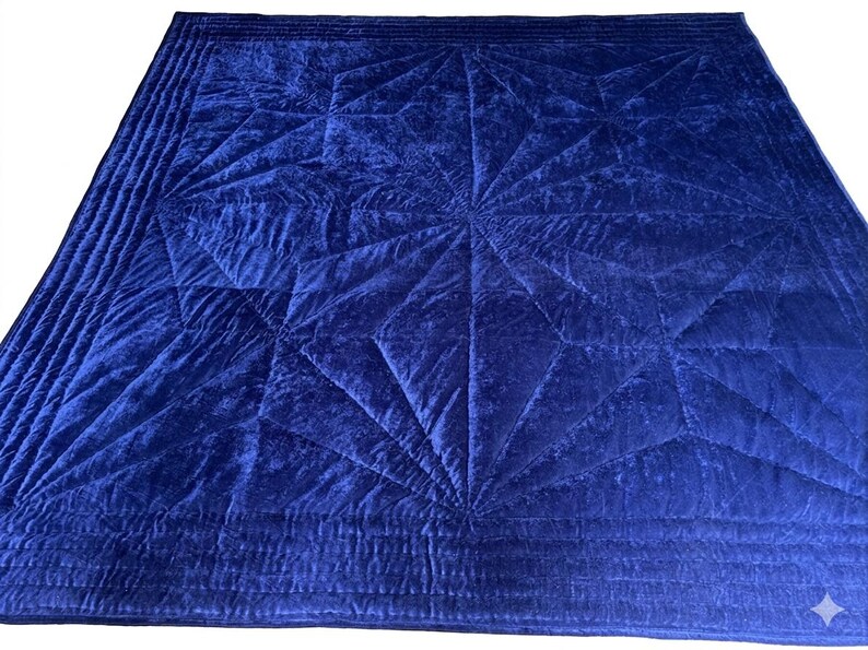 May include: A square, deep blue velvet quilt featuring a central geometric star pattern created by intricate stitching. The border consists of multiple parallel quilted lines that frame the central design, providing a textured appearance.