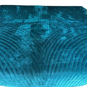 May include: A deep teal velvet quilt featuring a repeating pattern of curved, stitched lines that create a fan-like texture across the fabric. The material has a soft, reflective sheen, and the stitching forms geometric shapes throughout the surface.