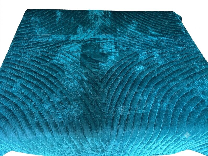 May include: A deep teal velvet quilt featuring a repeating pattern of curved, stitched lines that create a fan-like texture across the fabric. The material has a soft, reflective sheen, and the stitching forms geometric shapes throughout the surface.