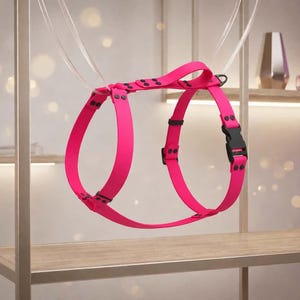 Peut inclure: Un harnais pour chien rose vif doté d'une conception à sangles lisses et flexibles avec des boucles en plastique noir, des curseurs réglables et des rivets métalliques. Le harnais comprend une poignée supérieure et un anneau en D pour la laisse.