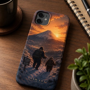 May include: A phone case featuring a scenic mountain landscape with two figures hiking. The case displays a sunset over a snow-covered mountain range, with the text "CALM ERA" at the bottom. The case is on a wooden surface.