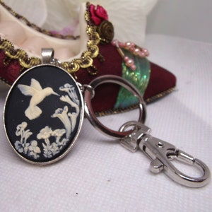 May include: A silver key chain with a black and white cameo featuring a hummingbird in flight. The cameo is oval shaped and has a white hummingbird with white flowers on a black background.