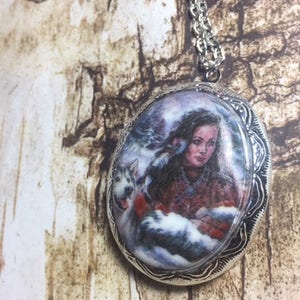 May include: A silver locket necklace with a white oval cameo featuring a woman with long dark hair and a dog in a snowy winter scene.