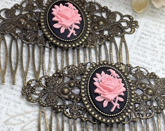 May include: Two antique bronze hair combs. Each comb features a pink rose cameo set on a black oval, framed by an ornate bronze filigree design. The combs have multiple tines for securing in hair.