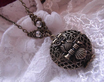 Puede incluir: Un collar de bronce de estilo vintage con un colgante redondo que representa un búho y un instrumento musical. El colgante tiene un diseño calado intrincado, y el collar incluye detalles decorativos con cristales transparentes.