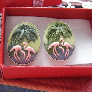 Peut inclure: Boucles d'oreilles ovales représentant une scène tropicale avec des flamants roses, des palmiers et de l'eau. Les boucles d'oreilles sont serties dans un métal argenté et présentées dans un coffret cadeau rouge.