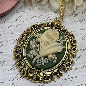 May include: A gold-tone pendant necklace with a green and white cameo featuring a lily of the valley design.