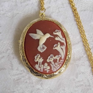 Può includere: Una collana con un ciondolo d'oro e un cammeo rosso con un colibrì bianco e fiori.