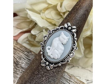 May include: A silver ring with a white cameo of a cat in a blue oval setting. The ring is on a wooden ring holder.