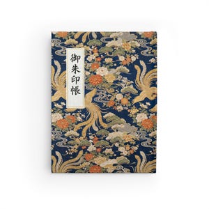 Puede incluir: Un cuaderno rectangular con una cubierta azul marino con un diseño tradicional japonés. El diseño incluye fénix dorados, flores y nubes. Una etiqueta rectangular blanca con texto japonés está en el lado izquierdo.