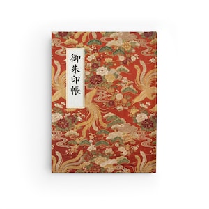 May include: A hardcover journal with a vibrant red background featuring a traditional Japanese pattern. The design includes golden phoenixes, flowers, and swirling water motifs. A white rectangular label with Japanese text is on the front.