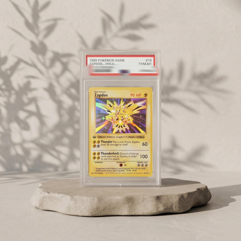 May include: A 1999 Pokemon Game Zapdos holographic trading card encased in a clear protective slab. The card features a yellow background, 90 HP, and the attacks Thunder and Thunderbolt. The label at the top reads 1999 POKEMON GAME ZAPDOS HOLO #16 GEM MT.