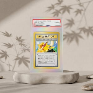 Puede incluir: Una tarjeta coleccionable hologr&aacute;fica japonesa "Pikachu Illustrator" de 1998, clasificada y sellada en una funda de pl&aacute;stico transparente. La tarjeta presenta una ilustraci&oacute;n de Pikachu sosteniendo un pincel y un bol&iacute;grafo, con el texto "ILLUSTRATOR" y caracteres japoneses.