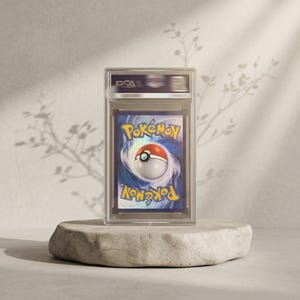 May include: A PSA graded Pok&eacute;mon trading card featuring the iconic blue and yellow logo with a central Pok&eacute; Ball graphic. The card is encased in a clear, rectangular protective plastic slab with the PSA logo clearly visible at the top section.