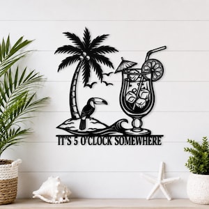 Puede incluir: Una pieza de arte mural de metal negro que presenta una escena tropical con una palmera, un tucán posado en una pequeña isla y una copa de cóctel con pajita y sombrilla. El texto "IT'S 5 O'CLOCK SOMEWHERE" aparece en la parte inferior.
