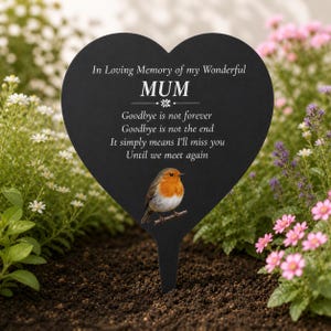 Peut inclure: Un piquet de jardin commémoratif noir en forme de cœur avec le texte "In Loving Memory of my Wonderful MUM". Un petit oiseau est perché sur une branche en bas. Le piquet est entouré de plantes vertes et de fleurs roses.