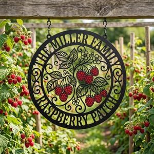 May include: A circular black metal sign featuring a cutout design of raspberry branches with leaves and berries. The text "THE MILLER FAMILY" is arched across the top, and "RASPBERRY PATCH" is arched across the bottom of the frame.