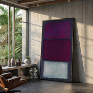 May include: Large framed abstract painting with three horizontal blocks of color: deep purple, maroon, and pale blue. The artwork leans against a concrete wall in a modern, sunlit room. A leather chair and decorative vases are visible.