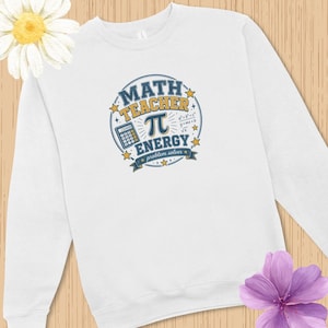 Könnte beinhalten: Ein weißes Langarm-Sweatshirt mit einer kreisförmigen Grafik und dem Text "MATH TEACHER ENERGY" in Blau und Gelb. Das Design enthält einen Taschenrechner, das Pi-Symbol, mathematische Formeln und kleine Sterne, mit "problem solver" darunter.