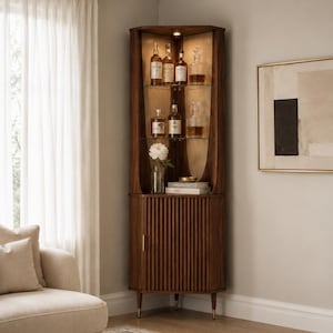 May include: A dark wood corner cabinet with glass shelves displaying liquor bottles and decanters. The cabinet has a ribbed door and brass-colored feet. A vase of white flowers sits on a shelf. The cabinet is in a well-lit room.