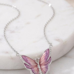 May include: A silver-toned butterfly pendant necklace. The butterfly has a gradient of pink and purple wings, outlined in silver, and accented with small, clear crystals. The necklace chain is delicate and silver.