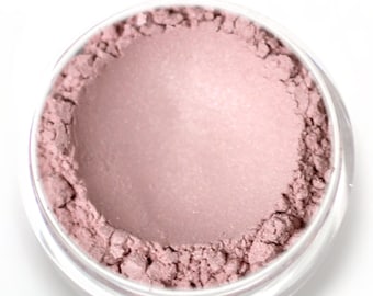 May include: A small, round container of loose, light pink eyeshadow with a shimmery finish.