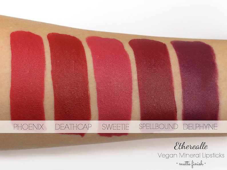 May include: Swatches of five matte finish vegan mineral lipsticks in shades of red and purple. The shades are named Phoenix, Deathcap, Sweetie, Spellbound, and Delphyne. The brand name Etherealle is also visible.
