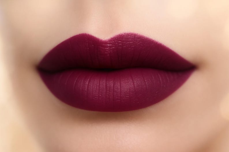 May include: Close-up of a person's lips painted with a deep burgundy lipstick. The lipstick has a matte finish and is applied evenly, highlighting the natural lip lines. The skin around the lips is smooth and fair.