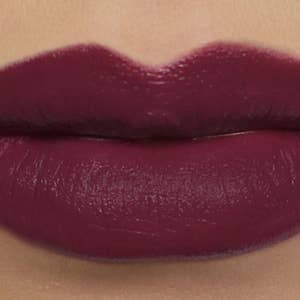 May include: Close-up of a person's lips, fully covered in a deep burgundy lipstick. The lipstick has a glossy finish, enhancing the rich color. The lips are well-defined, with a smooth and even application of the lipstick.