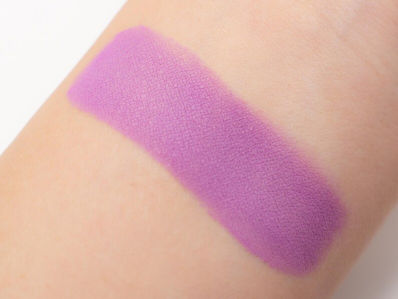 May include: A close-up of a light purple eyeshadow swatch on skin. The eyeshadow has a matte finish and is smooth and even.
