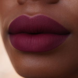 May include: Close-up of a person's lips painted with a matte, deep burgundy lipstick. The lipstick has a velvety texture and a rich, saturated color. The skin tone is dark, creating a striking contrast with the lip color.