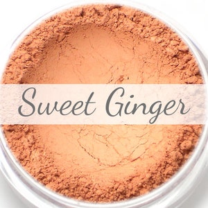 Può includere: Primo piano di un piccolo contenitore rotondo pieno di una polvere di colore arancio chiaro. Il contenitore è etichettato "Sweet Ginger".