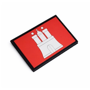 Könnte beinhalten: Ein rechteckiger Aufnäher mit dem Hamburger Wappen. Das Design zeigt einen roten Hintergrund mit einer weißen Illustration eines Schlosses und drei Sternen, umrahmt von einem schwarzen Rand.