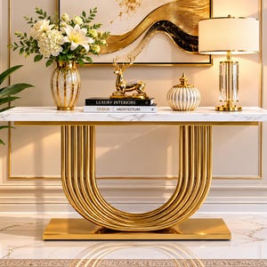 May include: A console table with a white marble top and a gold U-shaped base. On the table are a glass vase with white flowers, a gold deer figurine, two books titled Luxury Interiors and Design Architecture, a striped jar, and a gold lamp.
