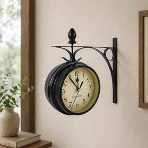 May include: A black, double-sided wall clock with a cream-colored face and black Roman numerals. The clock has a green inner rim and is mounted on a black metal bracket. The clock reads "NEW YORK" at the bottom.